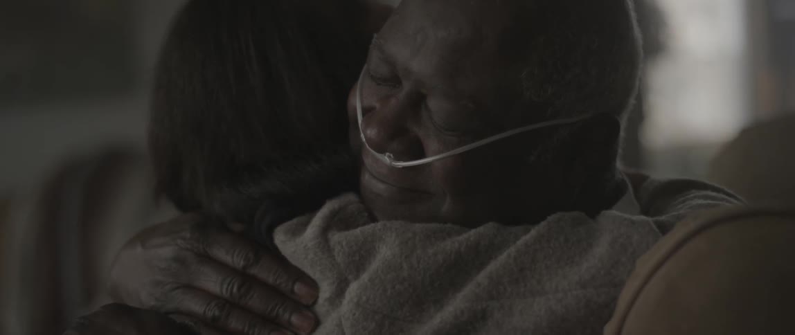 A woman hugs an elderly man with a breathing tube