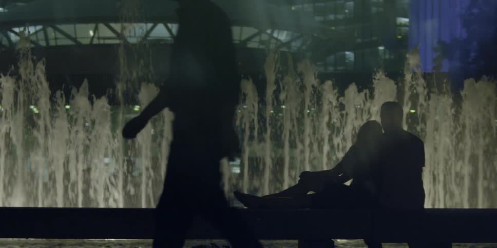 Silhouetted people watch a water fountain at night