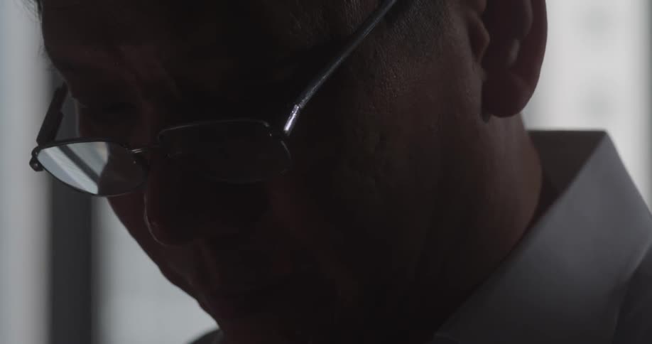 An older man with glasses looks down at something