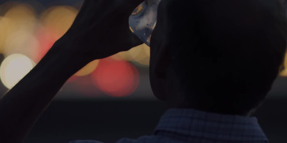 Man lifts a glass to his mouth and takes a drink