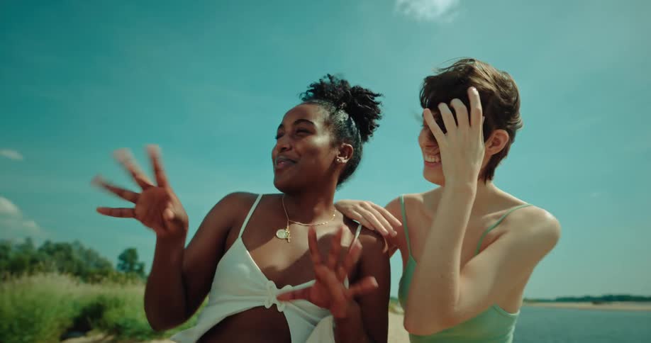 Two women stand outdoors on sunny day smile and gesture