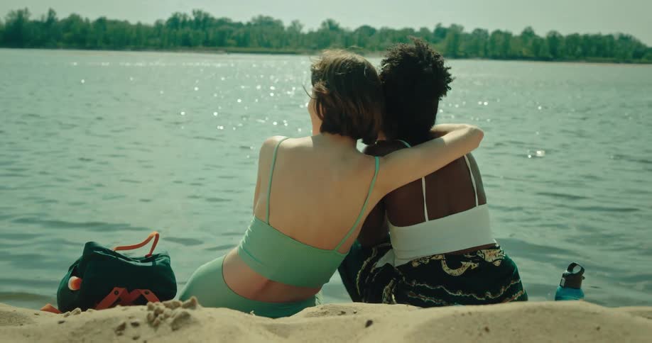 A female couple sitting on a beach hugging each other