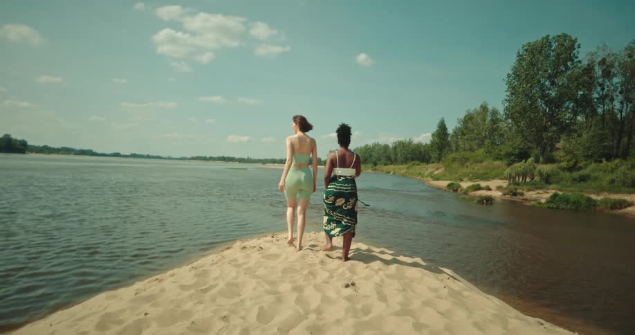 Two women walking towards the sand in the middle of a river smiling