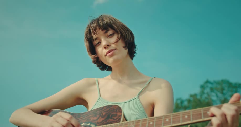 Woman strums her guitar and smiles as the trees sway gently in the breeze