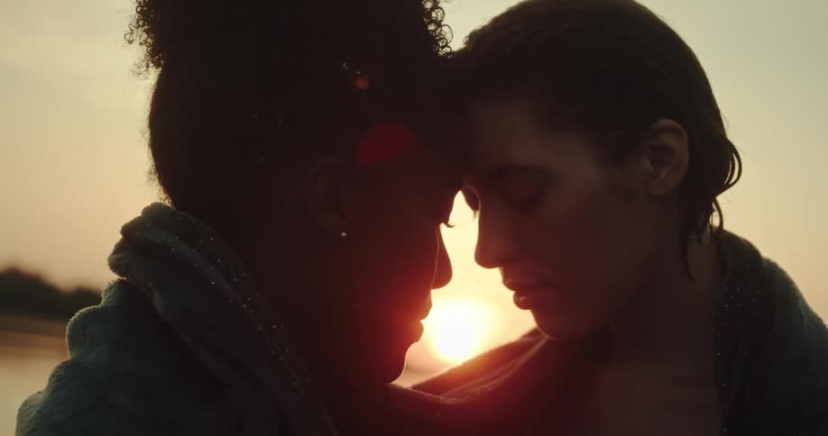 Two women leaning their foreheads together romantically with the sunset on the horizon