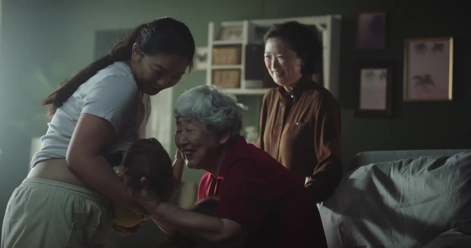 Three generations of asian women interact and hug toddler
