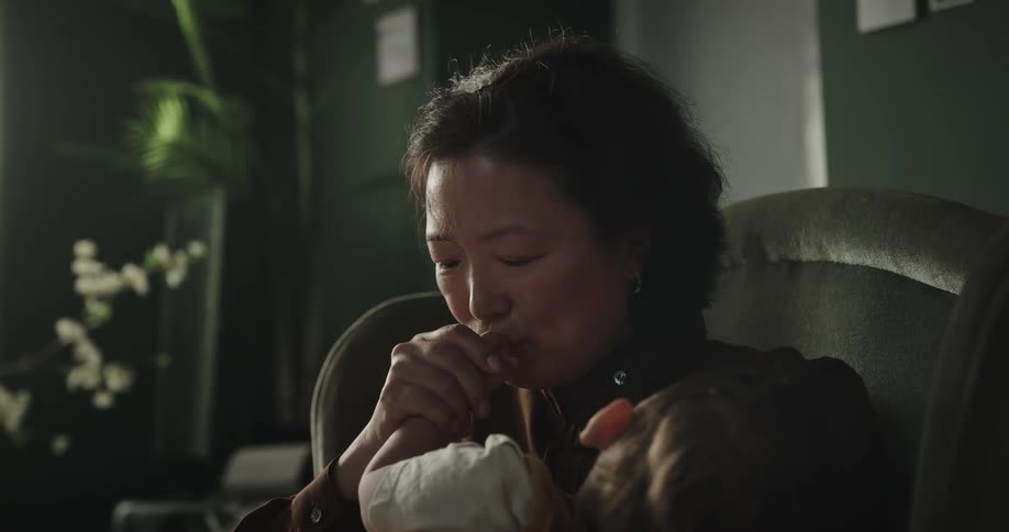 Grandmother sitting in an armchair with her grandson on her lap sleeping and her kissing his hand and face
