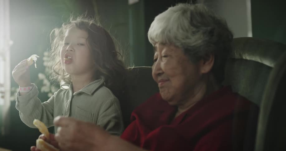 Grandmother eating an orange and helping her granddaughter eat an orange too