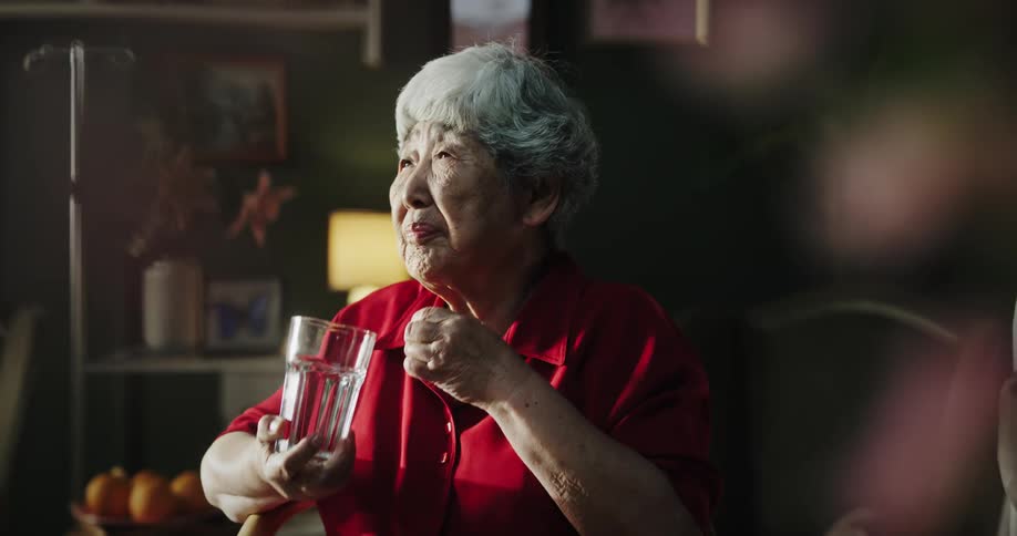Woman handing an elderly woman medicine and a glass of water as she drinks it