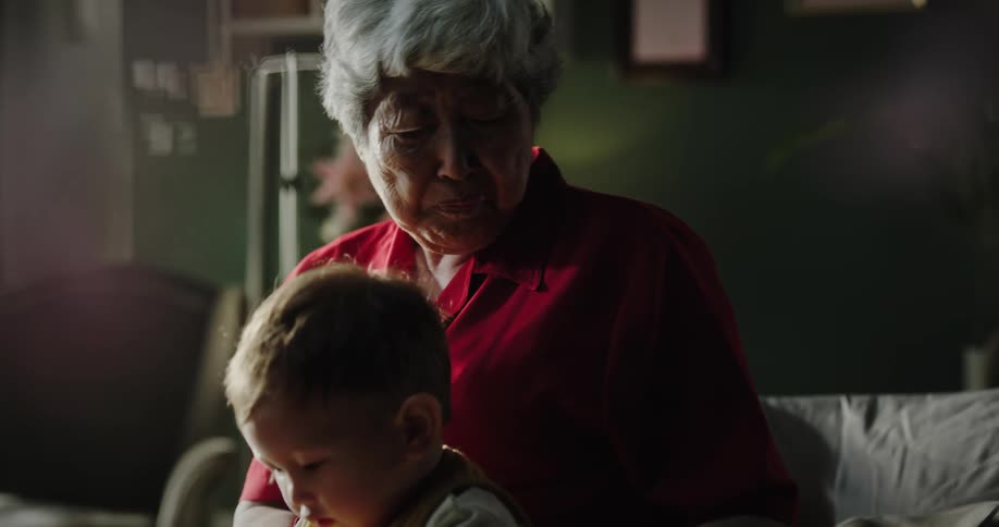 A sitting elderly woman is given a baby to hold