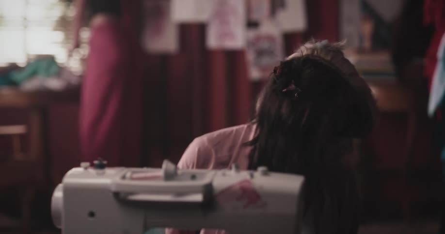 A woman was sitting and got up looking for clothes to sew on a sewing machine