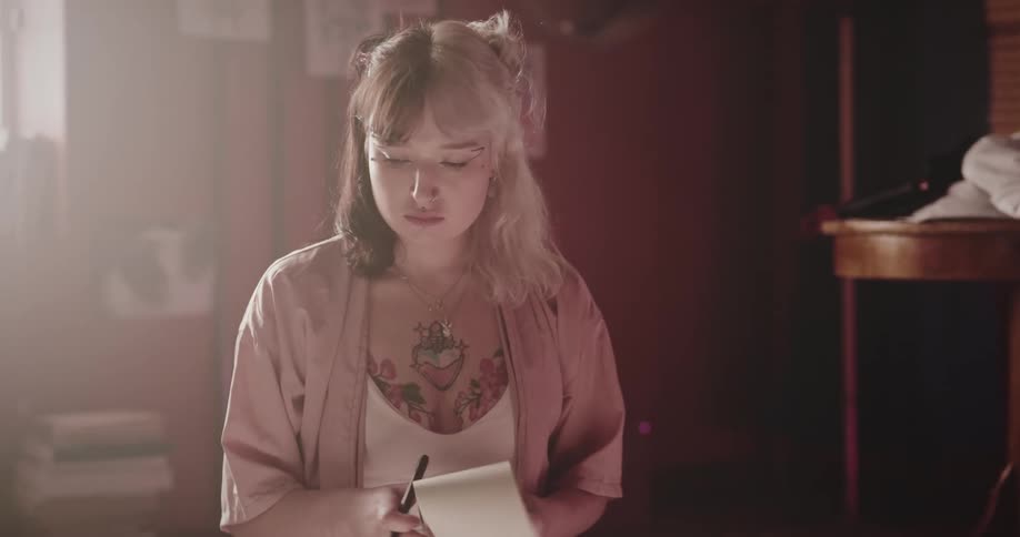 Woman with many tattoos writes on a notepad while sitting on the ground