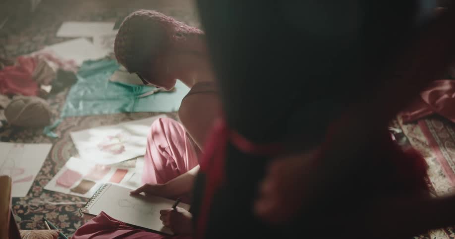 Woman sits on floor sketching on notebook