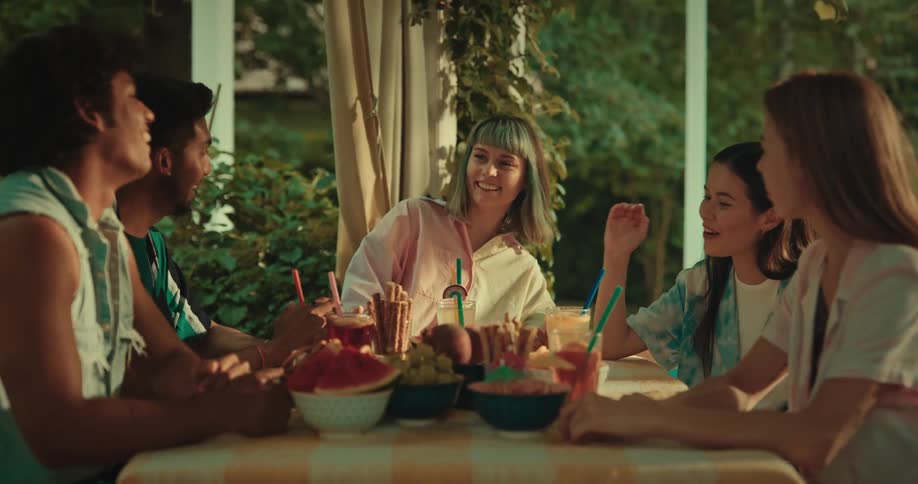A group of women and two men are sitting around a table with some food on the table and they are talking and smiling
