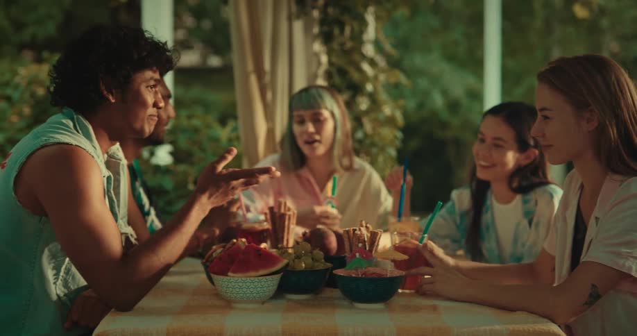 Several young people at a table with food are smiling and talking
