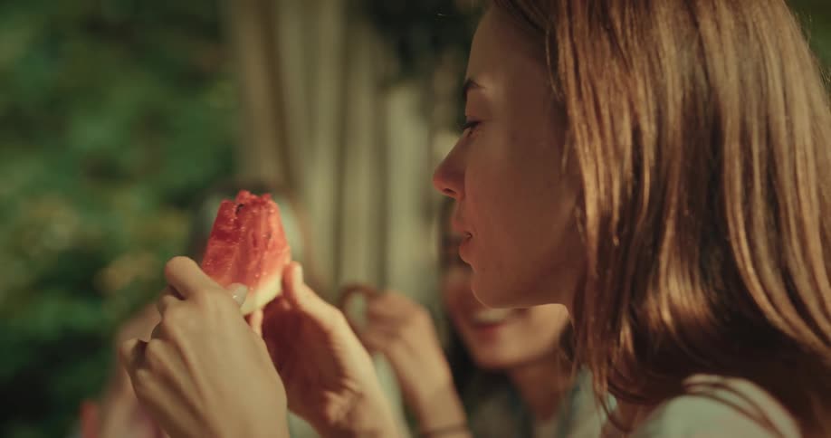 Woman eats a watermelon while enjoying a meal with friends outdoors