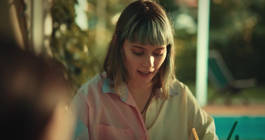 Friends sitting at a table with one of them writing on a white sheet of paper and playing
