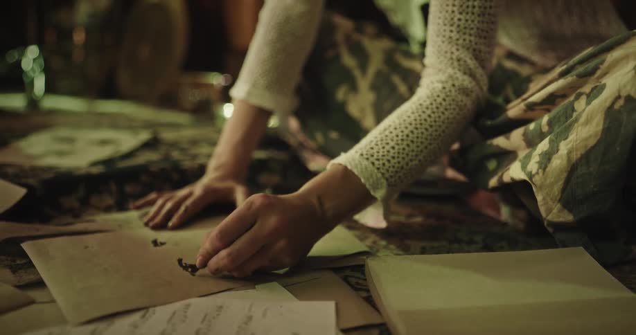 A young woman is sitting and pressing a black object on paper to paint it