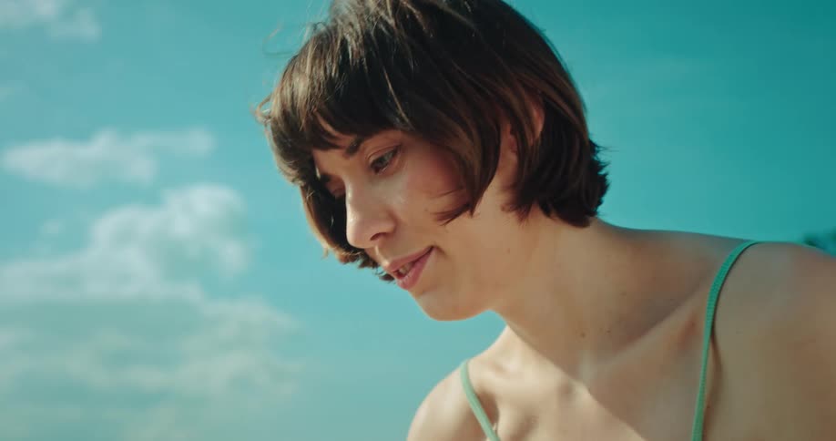 Woman with a light blue bikini looks down and smiles on the beach