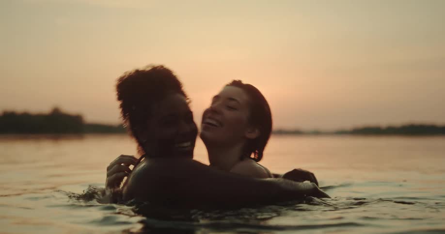 Two friends hugging inside the river with the sunset on the horizon