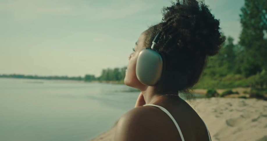 Black woman wearing headphones sways on beach