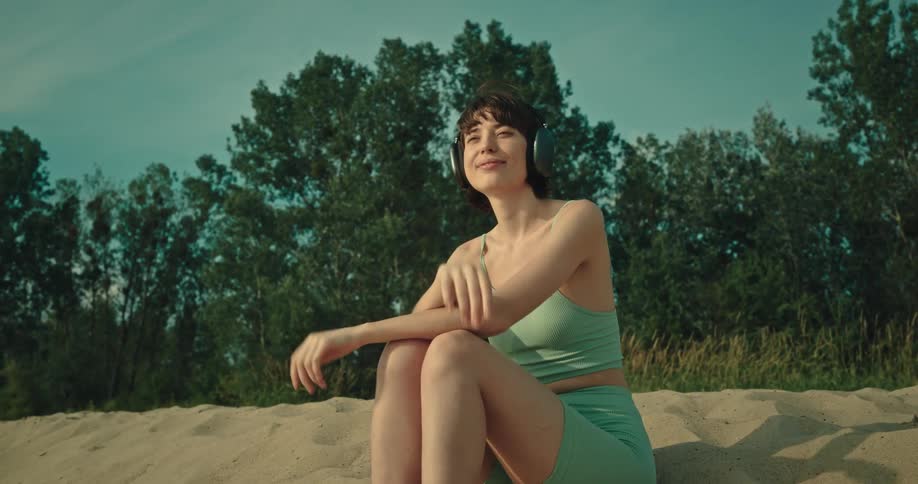 Woman sitting on the beach sand wearing headphones and enjoying