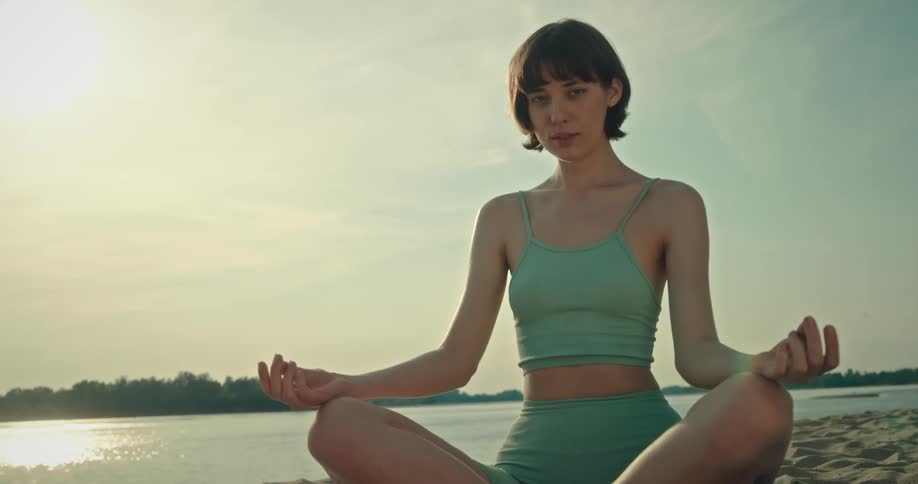 A young woman is sitting on the beach meditating