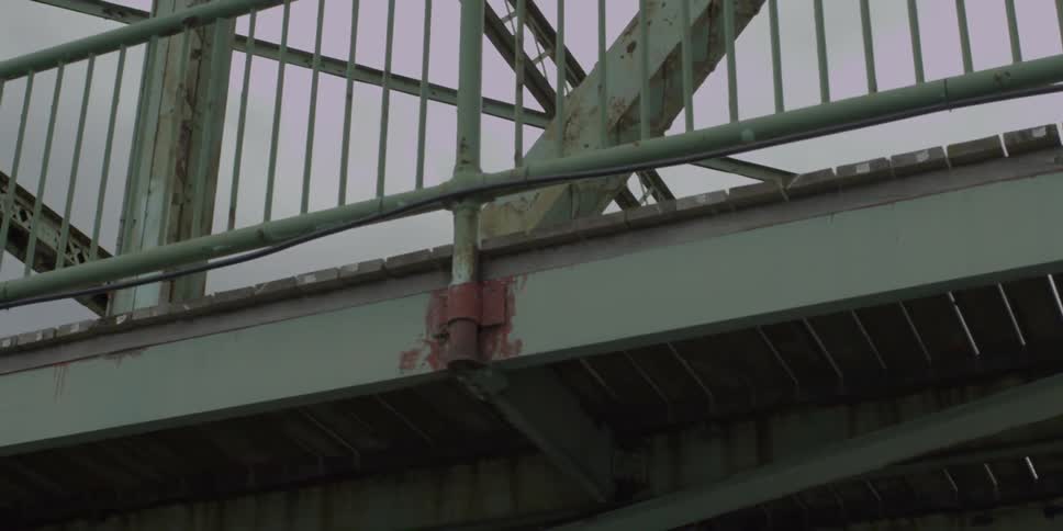 A rusty steel bridge towers above on an overcast day