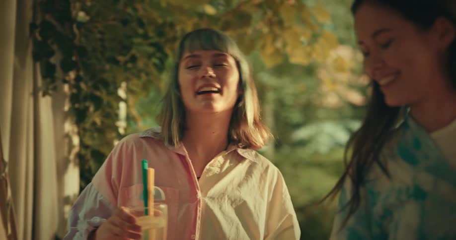 Small group of female friends laugh and drink together in a garden