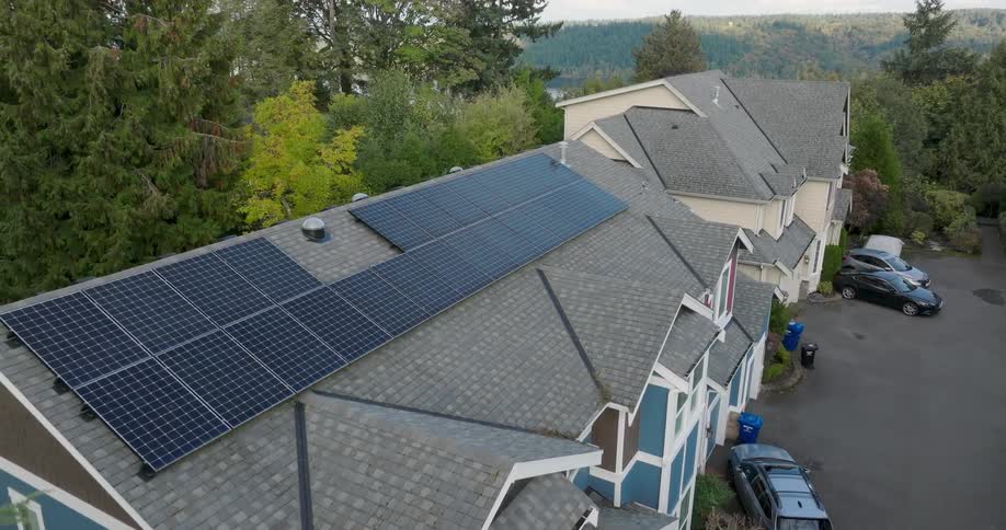Solar panels working on the pitched roof of modern townhomes in a tree filled suburban neighborhood