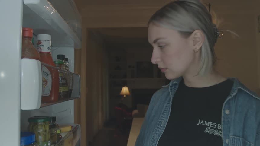 Blonde woman looks into refrigerator door bottles