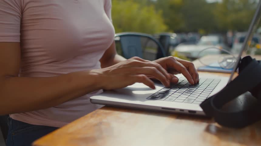 A woman is sitting at a table outside typing on a laptop computer