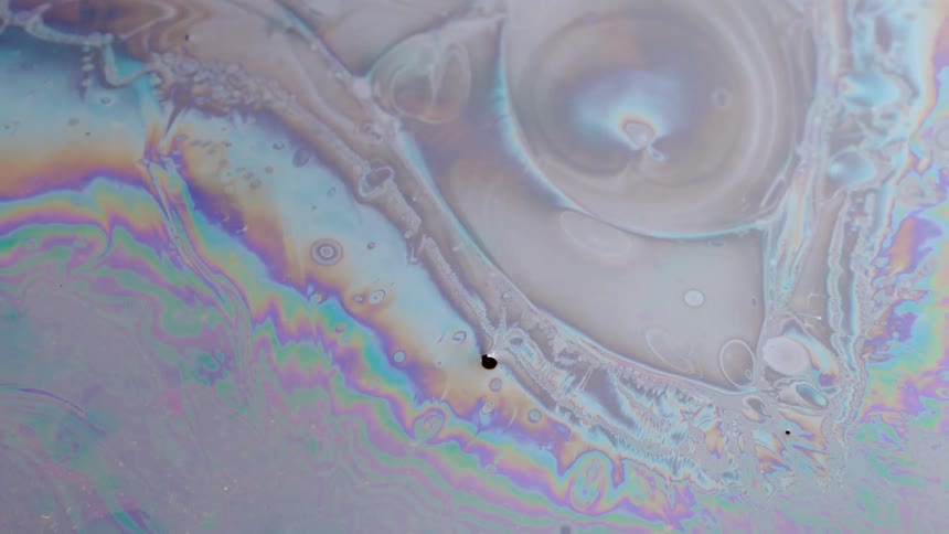 A white liquid moves and oily rainbow stripes spread over the substance