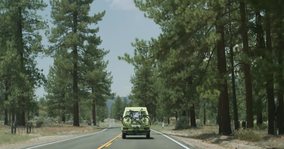 A truck with bicycles on back is traveling on a forest road with mountains in the distance