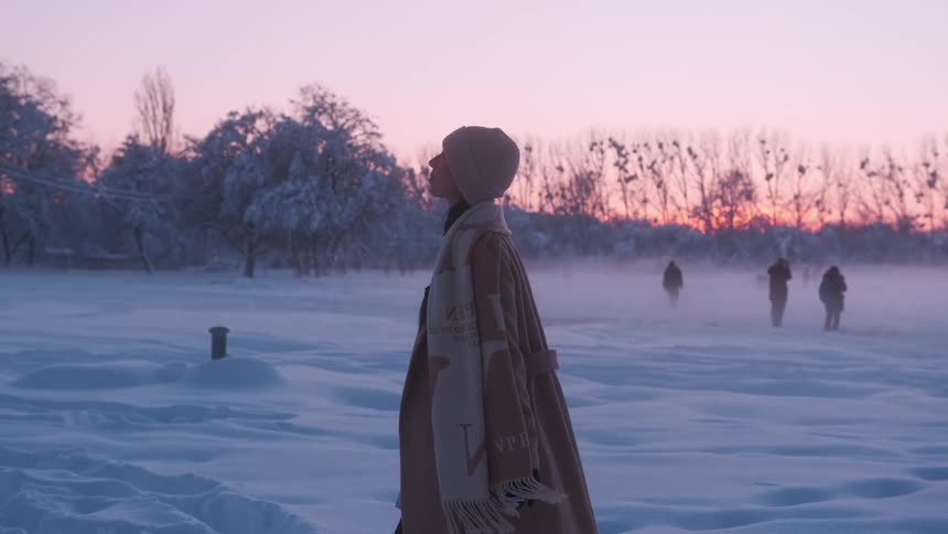 An elegant woman walking through the snow during sunset