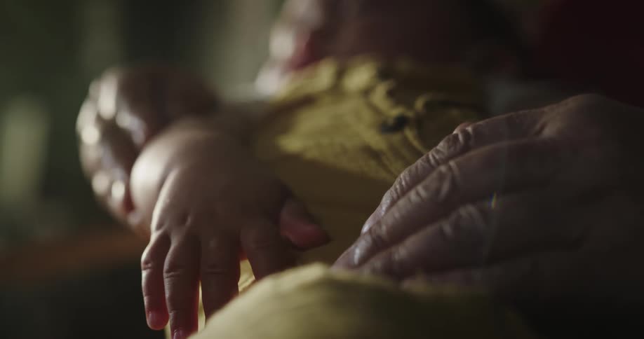 Elderly woman gengly squeezes the hand of a baby