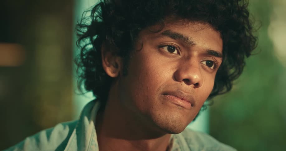 Man with curly hair and a light blue shirt talks with person smiling