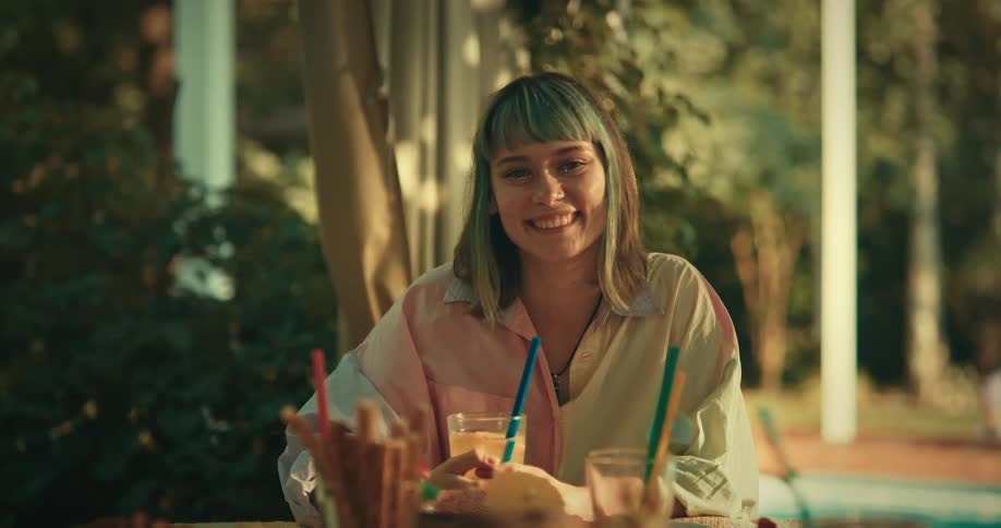 Woman sitting at a table sipping a drink with a straw and smiling