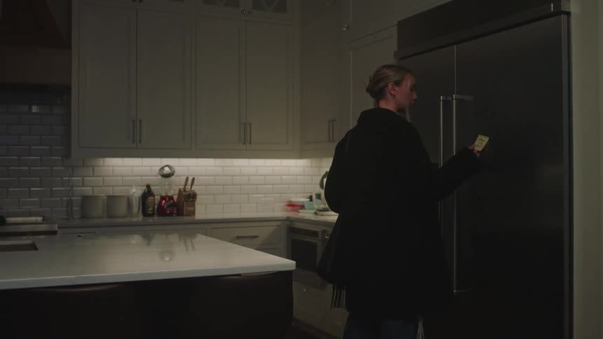 A woman reads a post it on the fridge