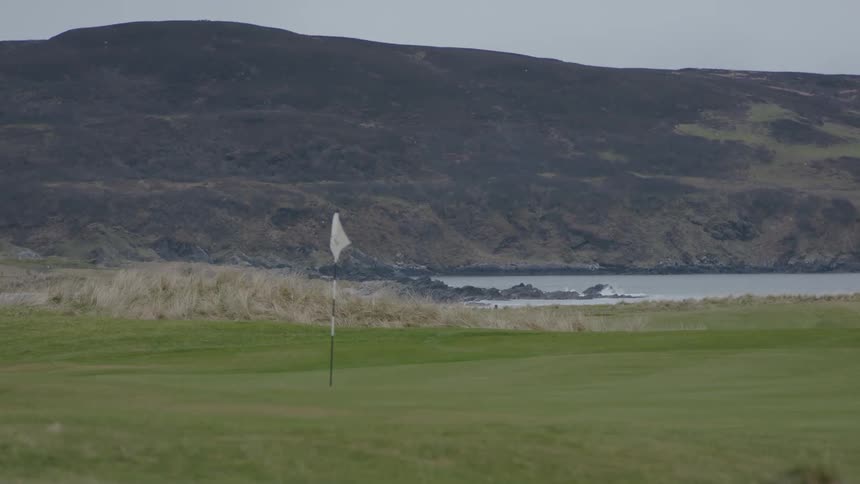 White flag marks the hole in the green on a golf course with a lake and hills in the background on a cloudy day