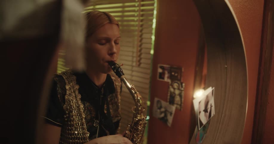 A woman is playing the saxophone and looking at herself in the mirror in a room