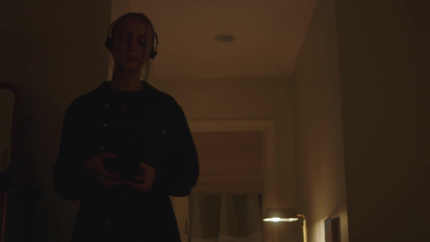 Woman walking in a dimly lit room while listening to music
