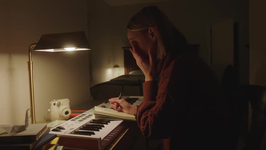 A young woman sits at her desk while writing in a small notebook