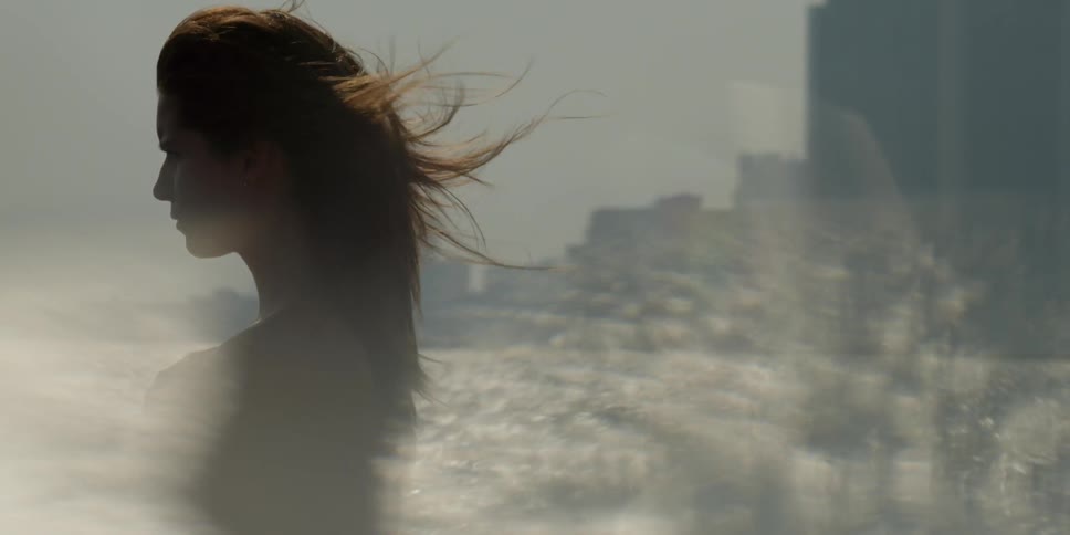 A woman's hair blows in the breeze while she stands near water