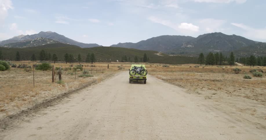 A truck with bicycles on back is traveling on a rural road with mountains in the distance