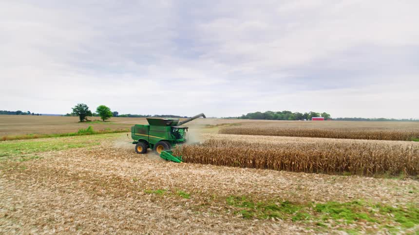 Drone shot of a tractor plowing a corn field under a cloudy sky