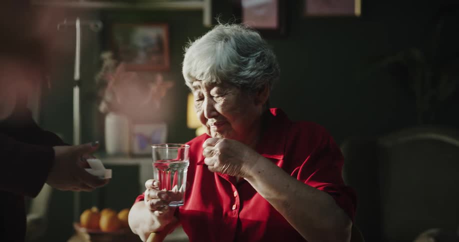 A younger woman hands medication and a glass of water to an elderly woman