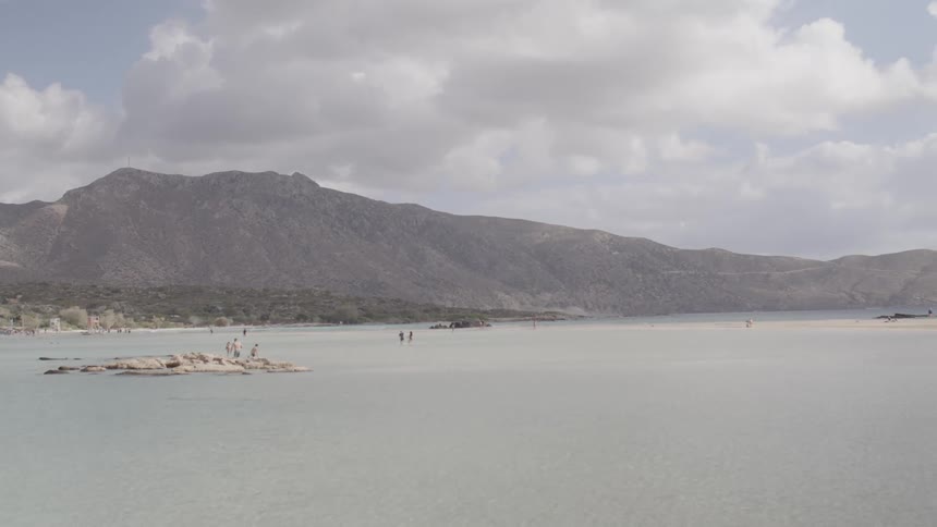 People play in the water and on the beach in front of mountains on a cloudy day