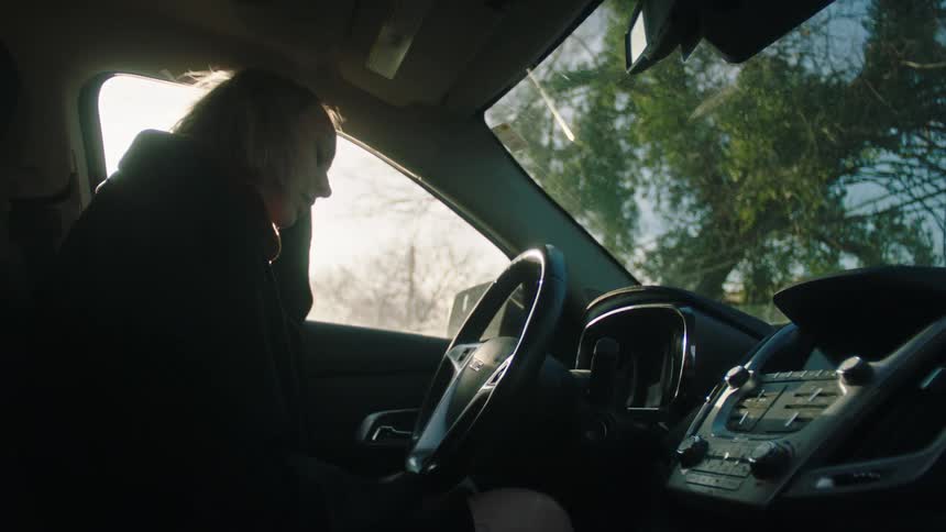 A woman closes the car door and grabs the steering wheel