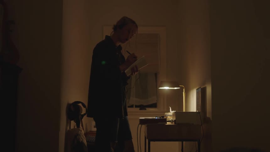 Woman standing and writing something in a notebook in a room at night
